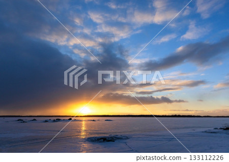 A tranquil winter scene shows a glowing sunset over a snow covered landscape A tranquil winter scene shows a glowing sunset over a snow covered landscape 133112226