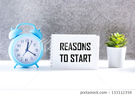 The phrase REASONS TO START in a notebook with an alarm clock and a flower on the table The phrase REASONS TO START in a notebook with an alarm clock and a flower on the table 133112356