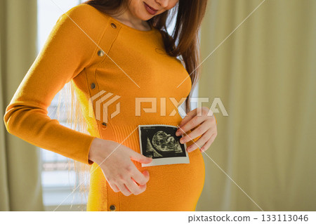 Prenatal ultrasound screening. Pregnant woman hands holding sonogram picture of unborn baby inside big belly. Happy expectant mom with fetus usi scan image. Young mother enjoying pregnancy. Maternity 133113046
