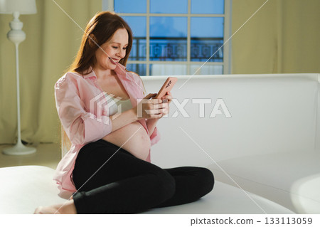 Pregnancy motherhood. Pregnant woman with smartphone typing scrolling at home. Woman with cell phone enjoying pregnancy surfing internet using social media apps. Mobile application for pregnant women Pregnancy motherhood. Pregnant woman with smartphone typing scrolling at home. Woman with cell phone enjoying pregnancy surfing internet using social media apps. Mobile application for pregnant women 133113059