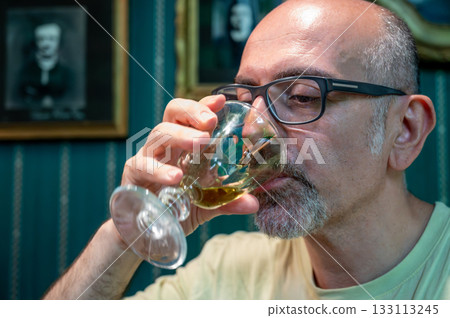 Prague, Czech Republic, August 8, 2023. Portrait of a middle-aged man drinking absinthe. Relaxation and meditation in a bohemian setting. Artistic lifestyle. 133113245