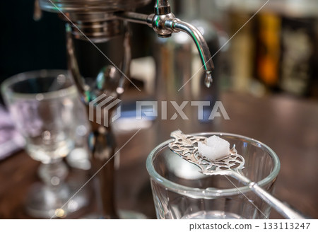 Prague, Czech Republic, August 8, 2023. From the tap of the still for making anise, drops fall onto a sugar cube placed on a special spoon, then into the glass. A fascinating preparation. 133113247