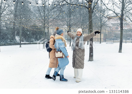 Group young adult smiling women wear long quilted coat white hat enjoy play snowball snowy day outdoors friends. Snowflakes fall playfully in front stairs decorated with glowing winter lights 133114386
