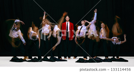 Leader standing still in red jacket while team moves chaotically around her in motion blur 133114456