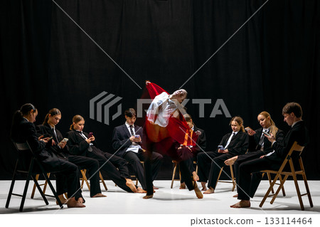 Expressive leap of performer in red jacket with motion-blur amid colleagues absorbed in smartphones 133114464
