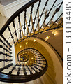 Spiral staircase viewed from above with wrought iron railing and warm pendant lights 133114485