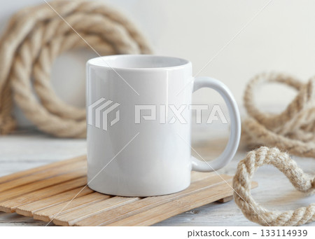 White ceramic coffee mug on wood against rustic jute ropes close up, nautical mockup 133114939