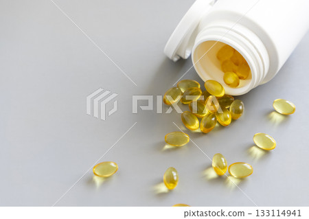 Yellow softgels (gelatin capsules) and bottle on a grey close up. Omega 3 Fish oil or garlic oil Yellow softgels (gelatin capsules) and bottle on a grey close up. Omega 3 Fish oil or garlic oil 133114941