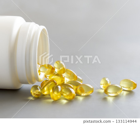 Yellow softgels (gelatin capsules) and bottle on a grey close up. Omega 3 Fish oil or garlic oil Yellow softgels (gelatin capsules) and bottle on a grey close up. Omega 3 Fish oil or garlic oil 133114944