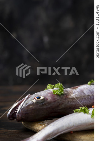 Fresh European hake fish on wooden board with parsley, Raw uncooked Merluccius merluccius close-up 133114948