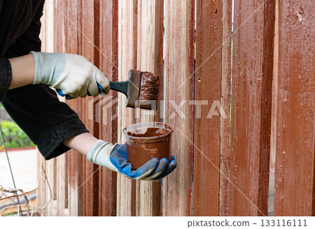Painting wooden fence with brown paint during daytime Painting wooden fence with brown paint during daytime 133116111