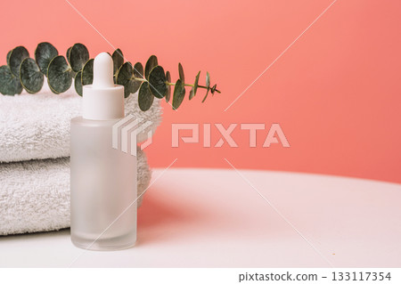 Serum bottle on soft towels with eucalyptus branch, pastel background 133117354