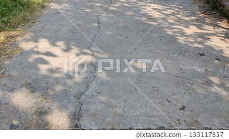 Shadow cast across cracked cement road showing urban wear and surface decay Shadow cast across cracked cement road showing urban wear and surface decay 133117857