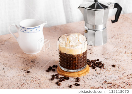 Iced creamy coffee into a glass with moka pot and milk jug on beige kitchen table Iced creamy coffee into a glass with moka pot and milk jug on beige kitchen table 133118070