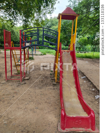 Colorful metal playground structure with ladders, yellow and green slides, climbing arches, and shaded platforms in outdoor park setting for children Colorful metal playground structure with ladders, yellow and green slides, climbing arches, and shaded platforms in outdoor park setting for children 133118186
