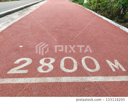Red jogging track with "2800 M" distance marker in park, synthetic running lane with clear milestone for fitness enthusiasts, promoting outdoor exercise and healthy lifestyle Red jogging track with "2800 M" distance marker in park, synthetic running lane with clear milestone for fitness enthusiasts, promoting outdoor exercise and healthy lifestyle 133118205