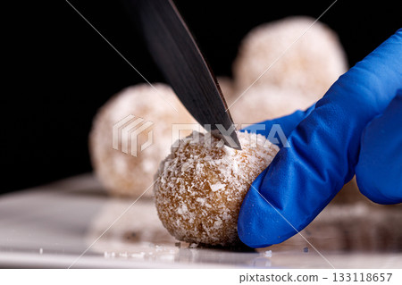 Beautiful sweets with coconut are cut with a knife on a white plate on a black background 133118657