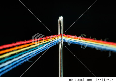 multi-colored threads for sewing in the form of a rainbow pass through an antique needle on a black background multi-colored threads for sewing in the form of a rainbow pass through an antique needle on a black background 133118697
