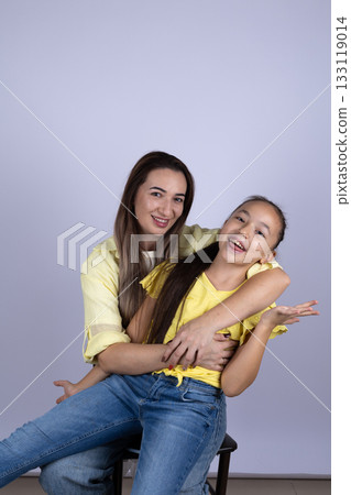 The woman is hugging the girl from behind, and they are both smiling happily 133119014