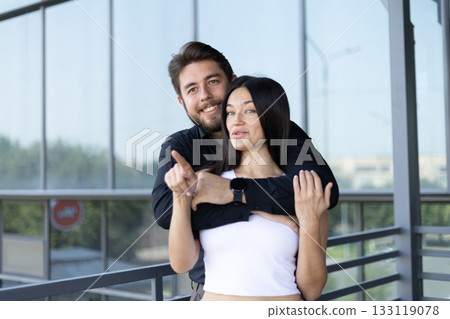 A man is hugging a woman from behind while pointing to something in the distance A man is hugging a woman from behind while pointing to something in the distance 133119078