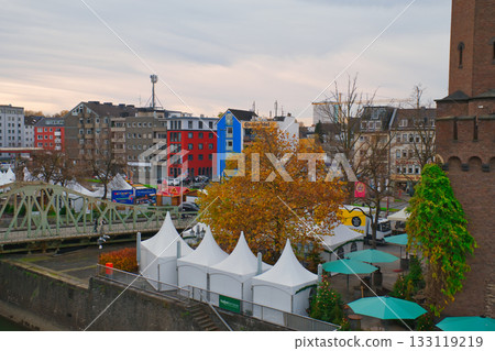 Colorful tents and autumn trees by the river in a vibrant city setting Colorful tents and autumn trees by the river in a vibrant city setting 133119219
