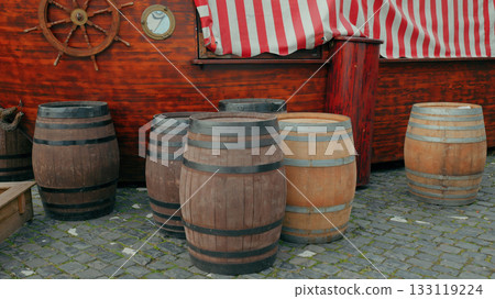 Wooden barrels arranged near a colorful striped boat at a waterfront market 133119224