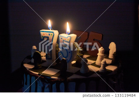 candles burning on a birthday cake with chocolate icing, chess pieces, the number 75 candles burning on a birthday cake with chocolate icing, chess pieces, the number 75 133119484