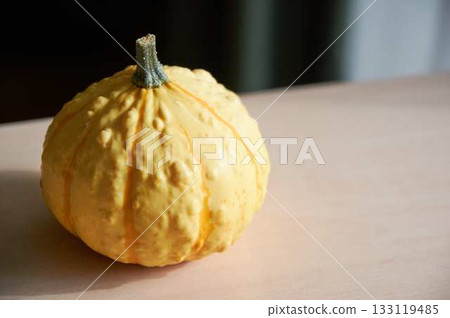 Yellow decorative pumpkin on a light-colored table with space for text. Holiday concepts, harvest. Yellow decorative pumpkin on a light-colored table with space for text. Holiday concepts, harvest. 133119485