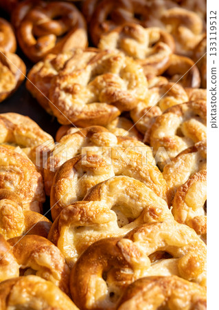 Crispy pretzels covered with melted cheese glow in warm sunlight, creating rich texture and golden surface. closeup view highlights baked crust, savory aroma  artisanal quality of freshly made snack 133119512