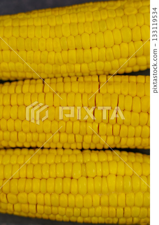 Close-up of yellow peeled ears of corn with large grains lying horizontally on a dark background in the center. The concept of healthy nutrition, natural iron, corn cultivation. High quality photo 133119534