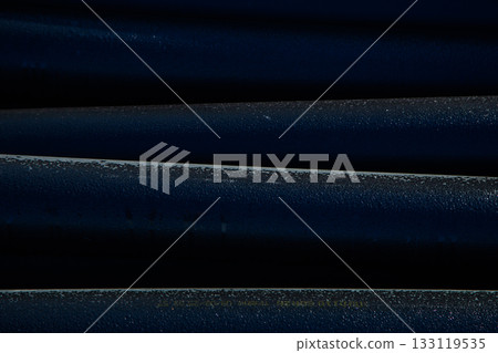 Parallel dark blue metal tubes with a textured surface create a striking visual composition that emphasizes industrial design and the play of light and shadow in a modern interior. High quality photo 133119535