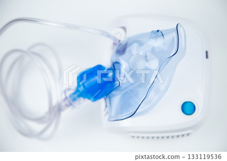 Top view of the breathing blue mask of the inhaler lying on the device out of focus on a white background. The concept of treating respiratory diseases, lung diseases, prevention and self-care. High 133119536
