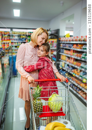 Mother and daughter hugging while grocery shopping in supermarket aisle 133119688