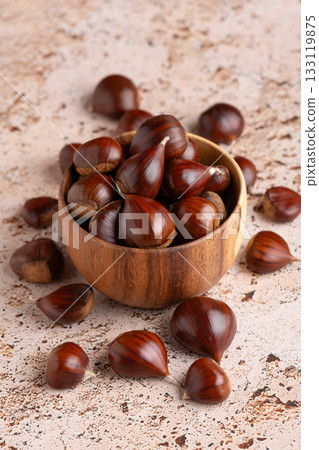 Autumn chestnuts in rustic wooden bowl on beige stone kitchen table 133119875