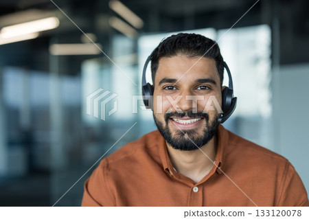 Young indian customer service agent with headset smiling confidently in modern office, providing friendly phone and online support as a professional call center representative 133120078