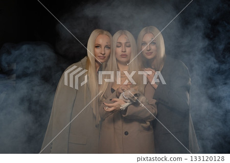 Three women with long blonde hair pose together in a smoky atmosphere at night 133120128