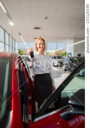 Happy young adult woman holding car keys at dealership 133120198