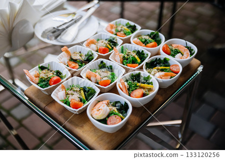 Mini shrimp seaweed salads in white bowls on a catering tray at an outdoor event Mini shrimp seaweed salads in white bowls on a catering tray at an outdoor event 133120256