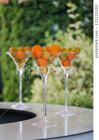 Elegant martini glasses filled with kumquats on a glossy bar outdoors, summer party vibe 133120260