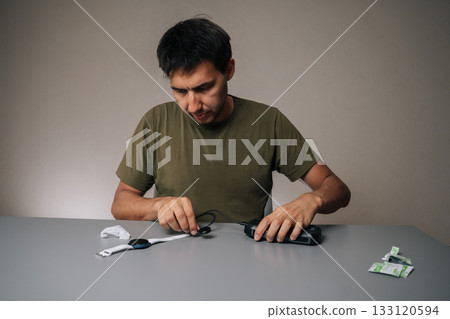 Front view of man connecting smartwatch to portable charger, preparing for outdoor activities, ensuring continuous functionality, sitting at table on isolated background. Concept of healthy lifestyle 133120594