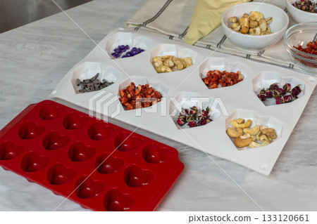 Heart-shaped silicone mold with nuts and dried fruit ingredients on kitchen counter 133120661