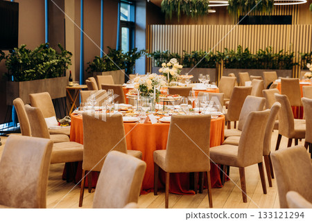 Elegant banquet hall with round tables, floral centerpieces and orange tablecloths 133121294