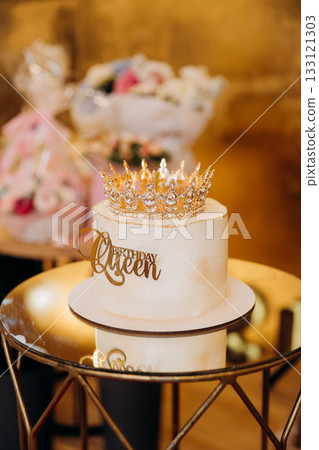 White birthday cake with golden crown and Birthday Queen topper on elegant party table White birthday cake with golden crown and Birthday Queen topper on elegant party table 133121303
