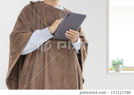 A man in his 30s using a tablet while wearing a wearable blanket (Japanese, no face) 133121786