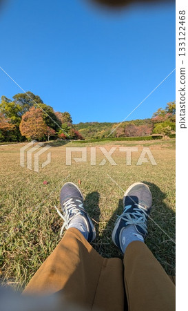 一位穿著運動鞋的人在公園草地上休息，可以欣賞秋葉美景。 133122468