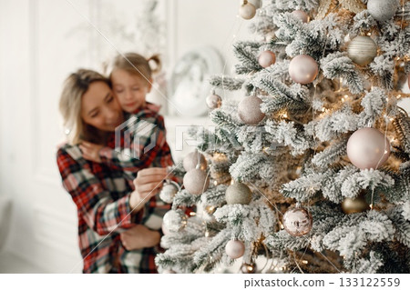 Blonde mother and little daughter in studio posing for a photo. Woman and daughter wearing plaid pajamas. Family celebrating Christmas together. Blonde mother and little daughter in studio posing for a photo. Woman and daughter wearing plaid pajamas. Family celebrating Christmas together. 133122559