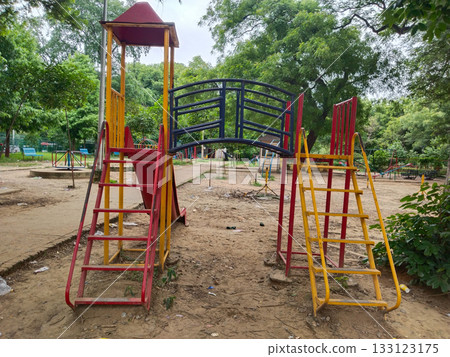 Colorful metal playground structure with ladders, yellow and green slides, climbing arches, and shaded platforms in outdoor park setting for children 133123175