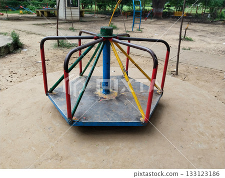Colorful metal roundabout or merry go round with red, blue, green seats in outdoor park playground, fun and engaging group equipment for children 133123186