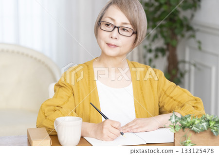 Senior woman writing an end-of-life note in the living room 133125478