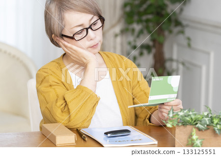 一位老婦人在客廳看著她的臨終遺書和存摺。 一位老婦人在客廳看著她的臨終遺書和存摺。 133125551